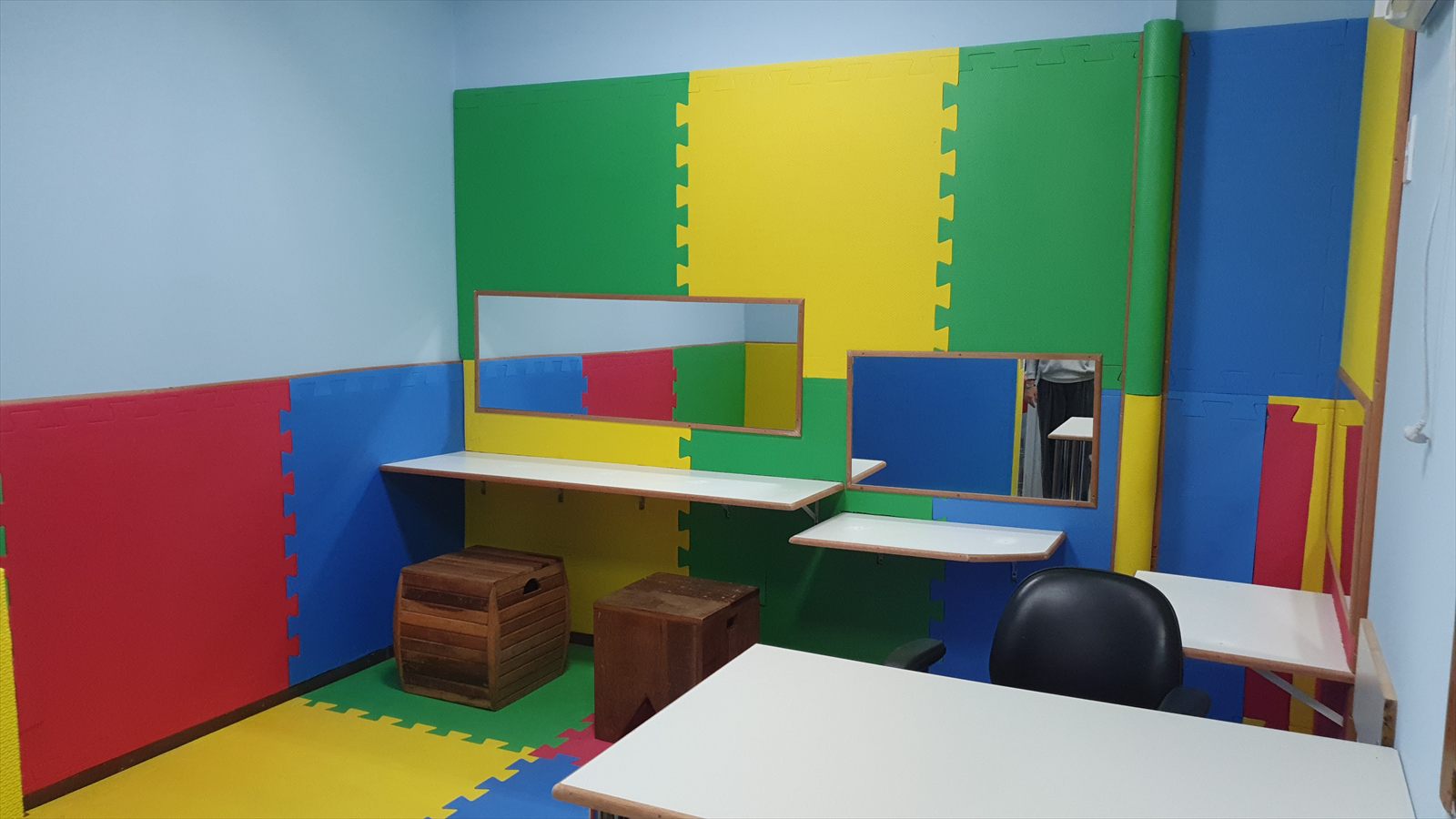 Sala de psicomotricidade da clínica, revestida com tatames coloridos, espelhos e bancadas de apoio