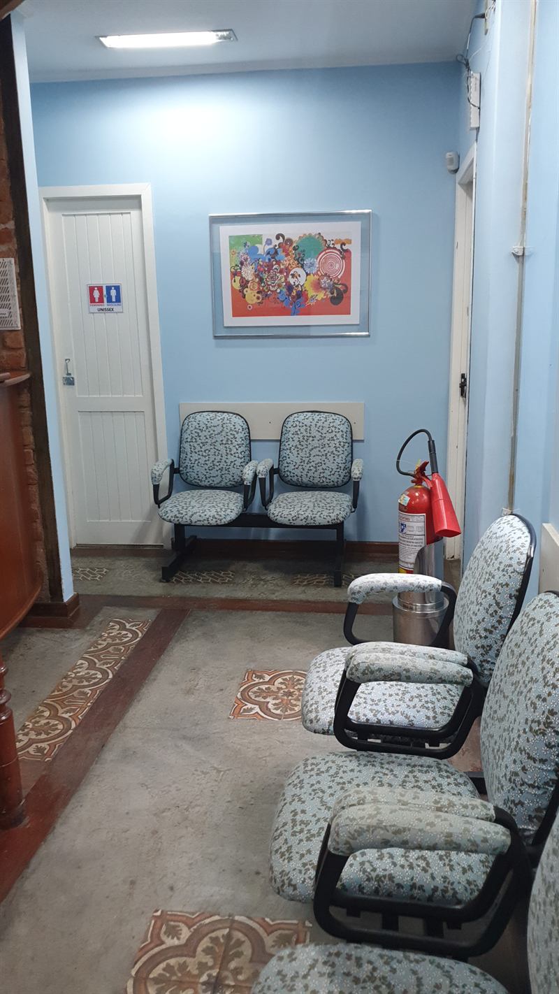 Sala de espera da clínica, com poltronas estofadas, quadro colorido e piso em ladrilho hidráulico